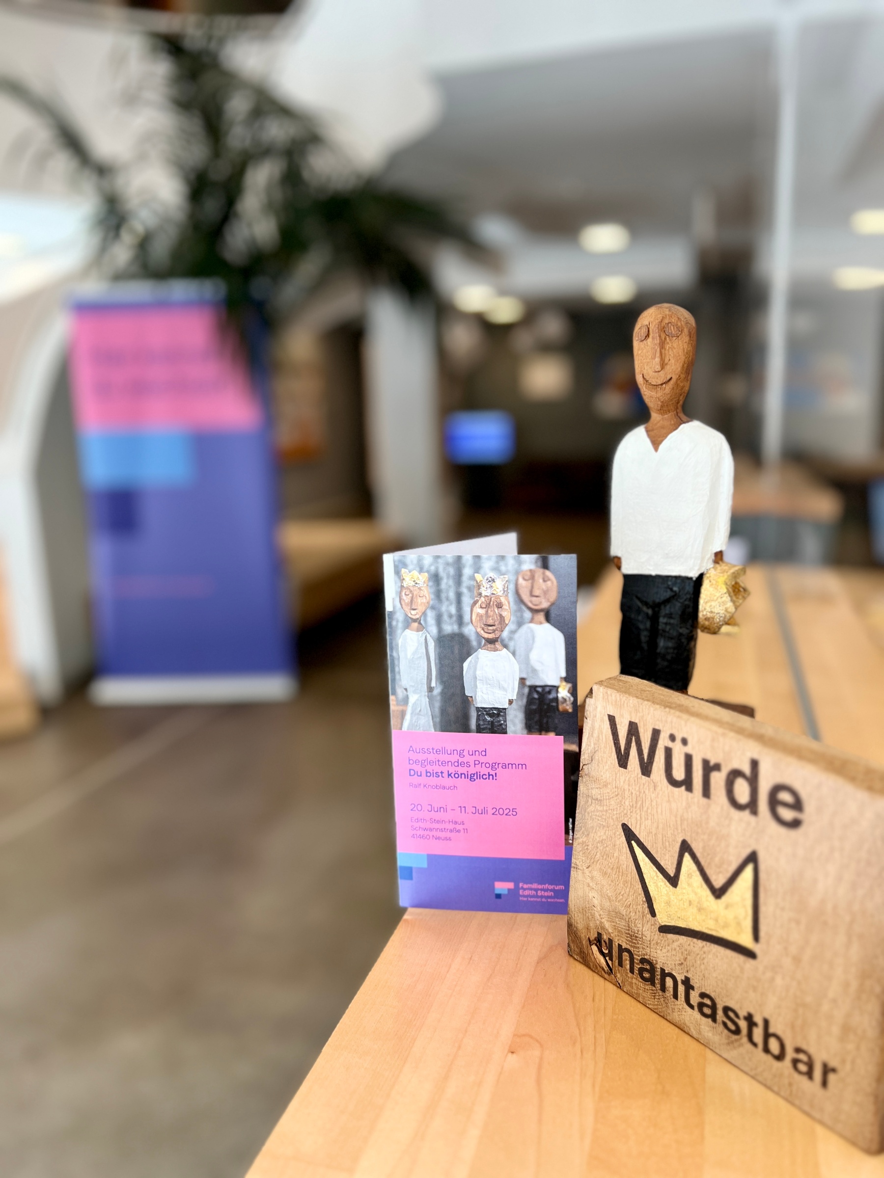 Holzskulptur eines Königs mit Krone in der Hand, Broschüre zur Auststellung und ein Holzschild mit der Aufschrift 'Würde unantastbar'