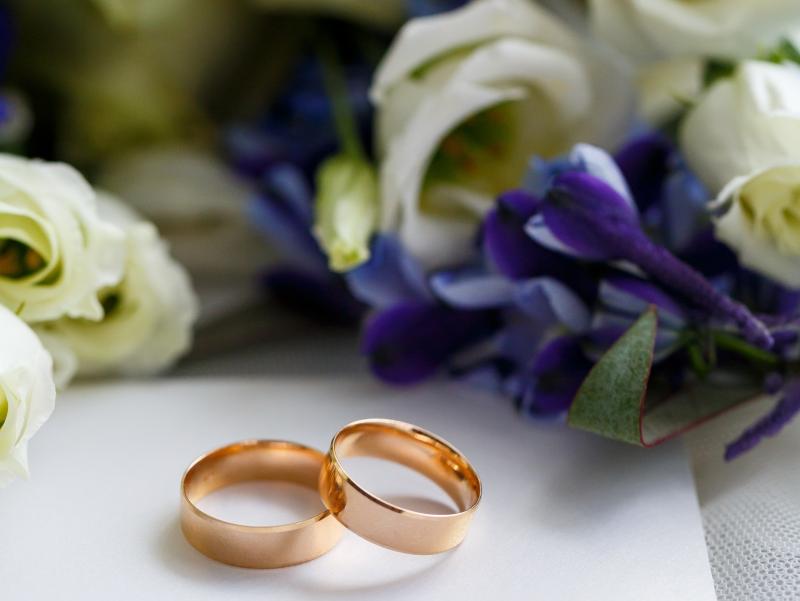Zwei Eheringe liegen vor einem Blumenstrauß