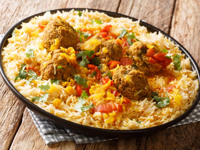 Auf einem Holztisch steht ein dunkler Teller mit einem Reisgericht.