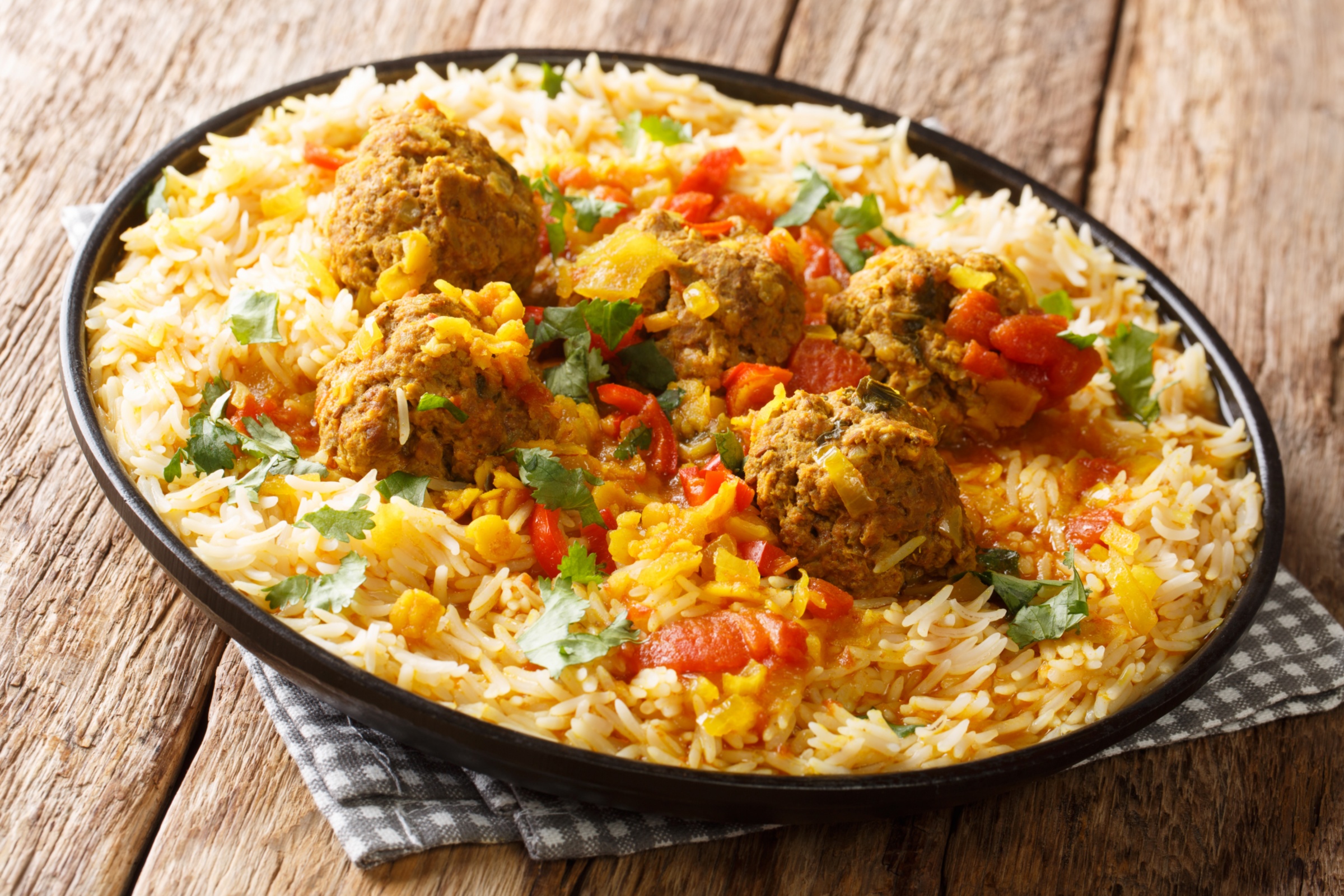 Auf einem Holztisch steht ein dunkler Teller mit einem Reisgericht.