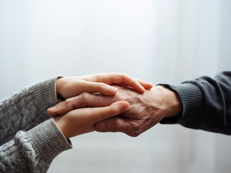 Beide Hände einer jüngeren Person halten die Hand einer älteren Person.