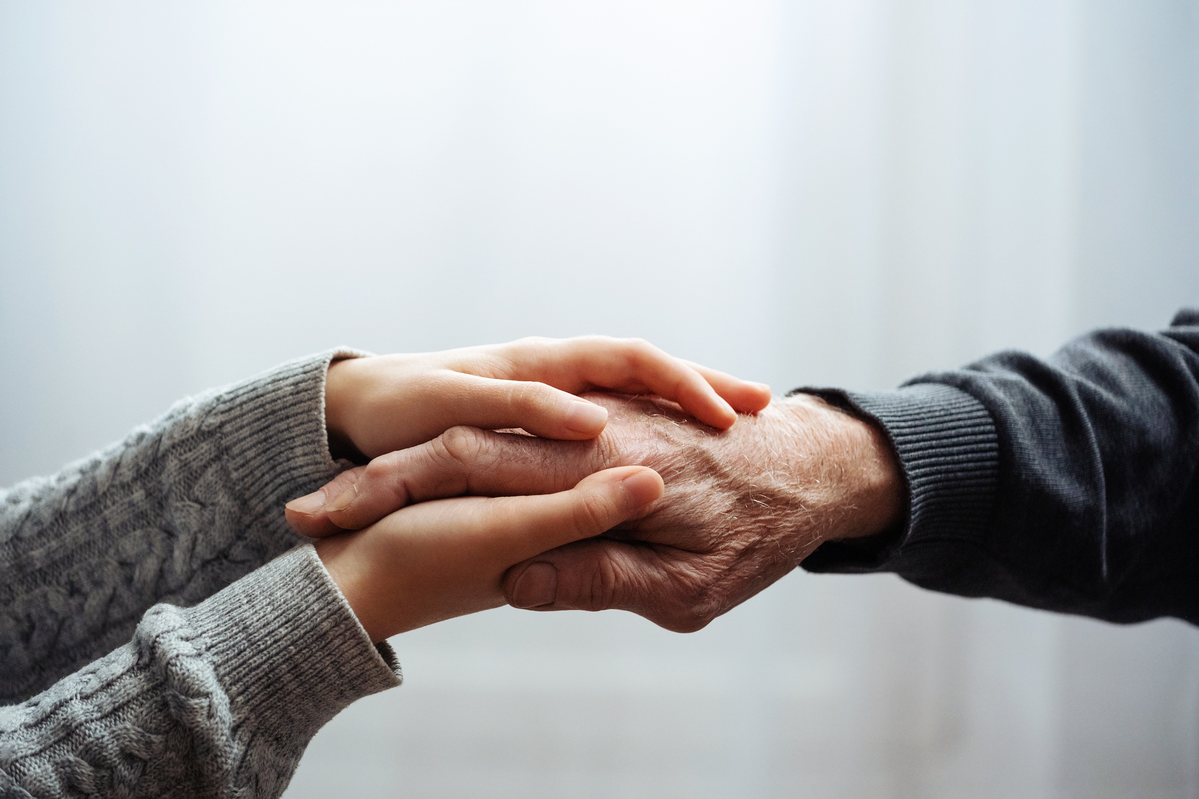 Beide Hände einer jüngeren Person halten die Hand einer älteren Person.