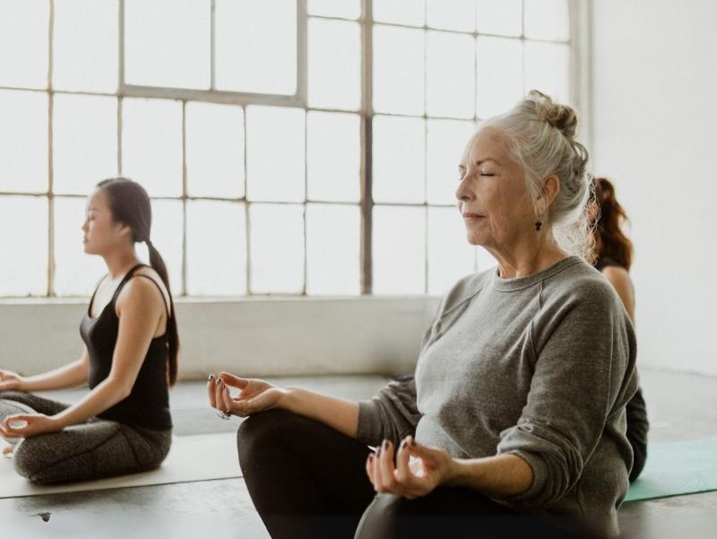 Drei Frauen sitzen in einer Yoga-Position in einem hellen Sportraum.