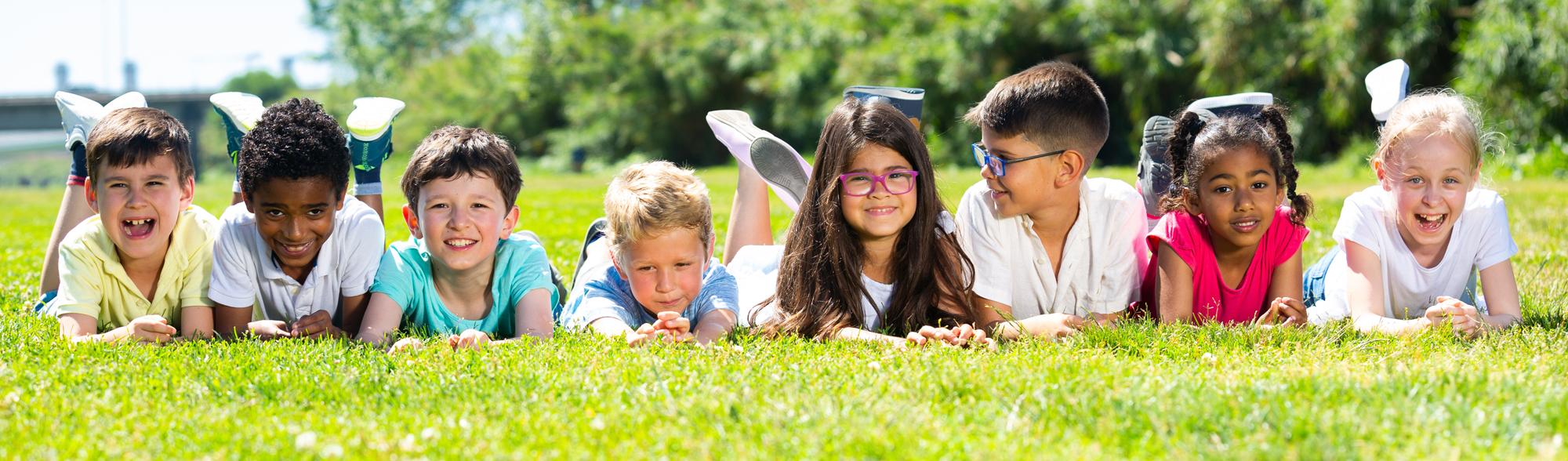 Happy team of friends children resting on grass together in park