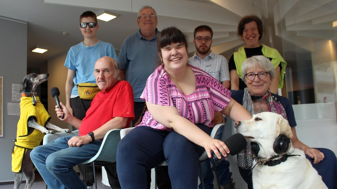 Gruppenbild der inklusiven Radioredaktionsgruppe Neuss All-in gemeinsam mit ihren Hunden auf der Galerie des Edith-Stein-Hauses.